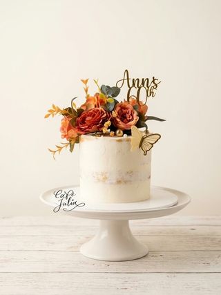 Ivory cake for Ann’s 60th birthday with orange flowers and a gold butterfly, displayed on a white cake stand.