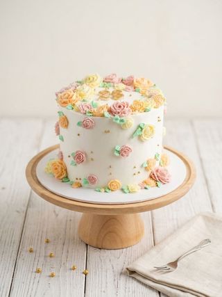 Ivory anniversary cake decorated with pastel buttercream flowers, tiny gold pearls, and two gold rings