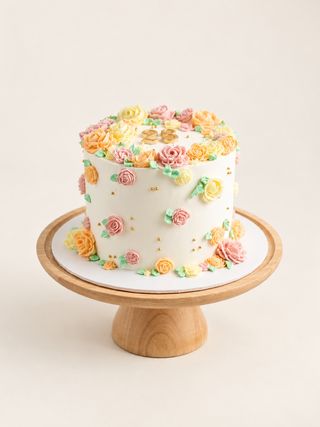 Ivory anniversary cake decorated with pastel buttercream flowers, tiny gold pearls, and two gold rings