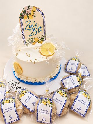 Zoe’s white 25th birthday cake with lemon decorations, blue piping, matching wrapped favors, and a Café Julia watermark