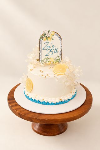 Lemon-themed cake for Zoe’s 25th birthday on a wooden stand against a warm ivory background
